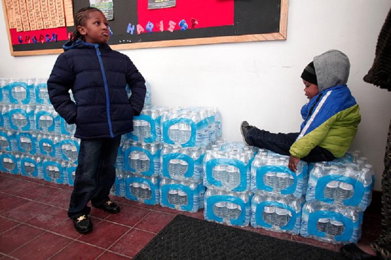 Justin Roberson (L), age 6, of Flint, Michigan and Mychal Adams, age 1, of Flint wait on a stack of bottled water at a rally where the Rev. Jesse Jackson was speaking about about the water crisis.
