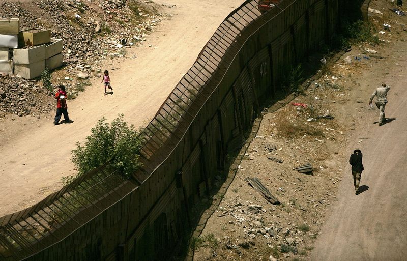 People walk past each other on opposite sides of the fence along the U.S. Mexican border