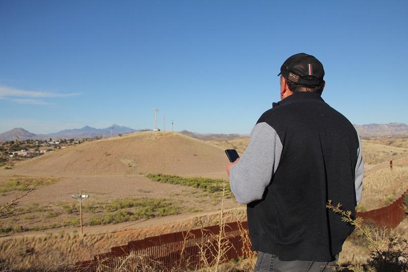 "Comanche," a Sinaloa cartel boss who oversees an illegal smuggling cell in Nogales, Sonora, Mexico, looks over the border wall at a US Border Patrol surveillance truck atop a hill in Arizona.