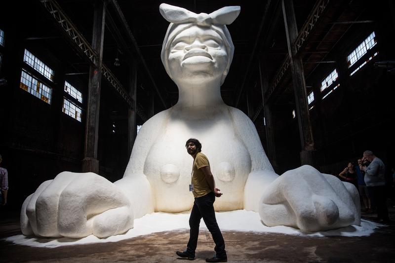 People view Kara Walker's 'A Subtlety,' a seventy-five and a half feet long and thirty-five and a half feet tall sphinx made in part of bleached sugar at the former Domino Sugar Refinery.