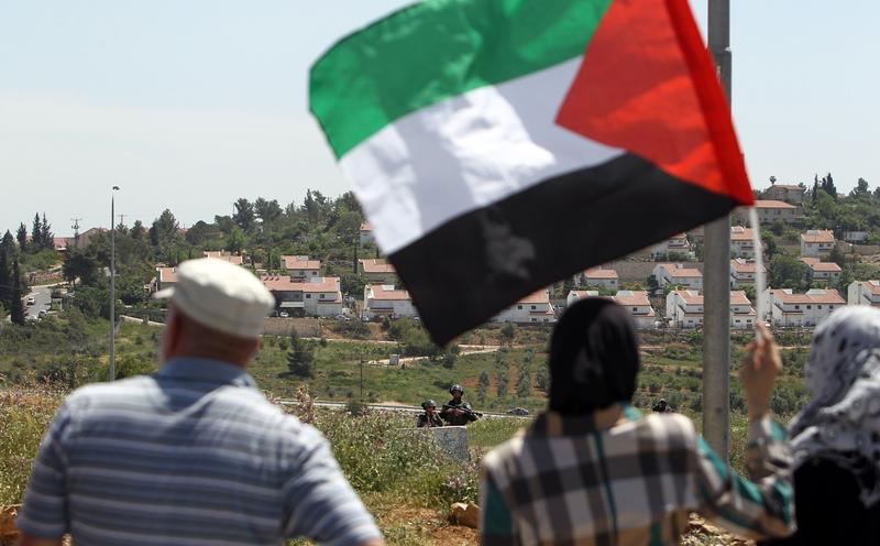 Palestinian protesters wave the national flag as they face-off with Israeli soldiers following a weekly demonstration against the expansion of settlements in the West Bank, on April 25, 2014.